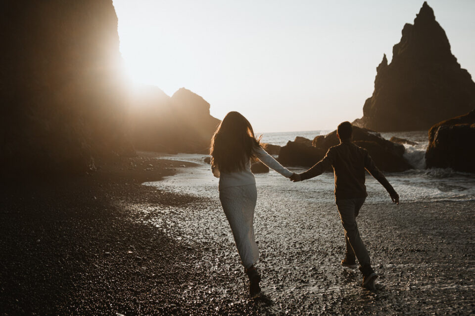 Energetic elopement couple playfully running towards the rising sun on Reynisfjara beach