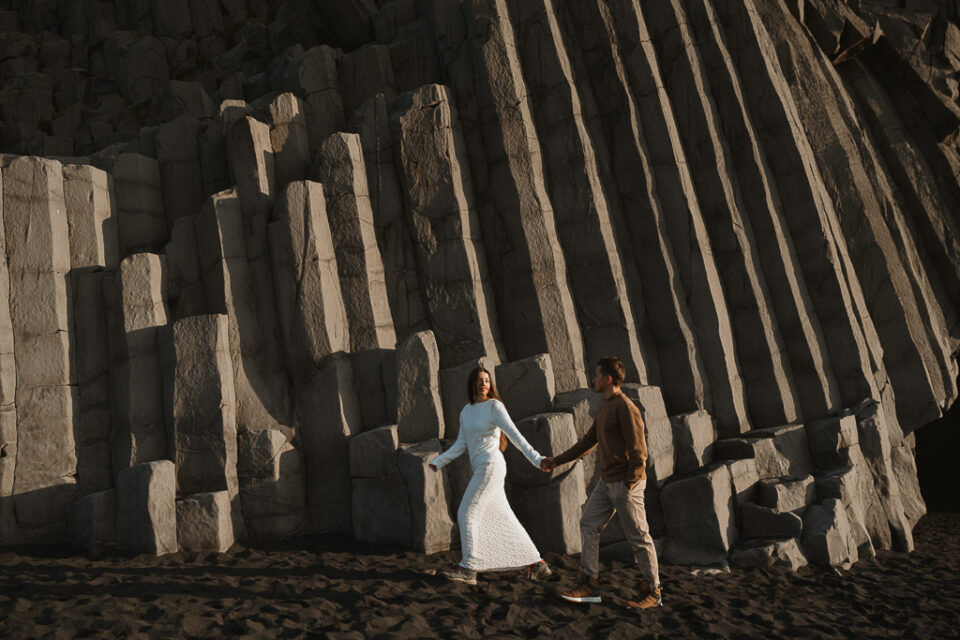 Whimsical moment as the couple wanders hand in hand among Reynisfjara's mesmerizing basalt formations