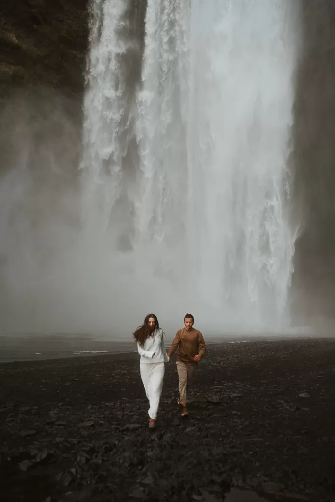 Elopement couple running captured against the backdrop of Skogafoss' cascading water