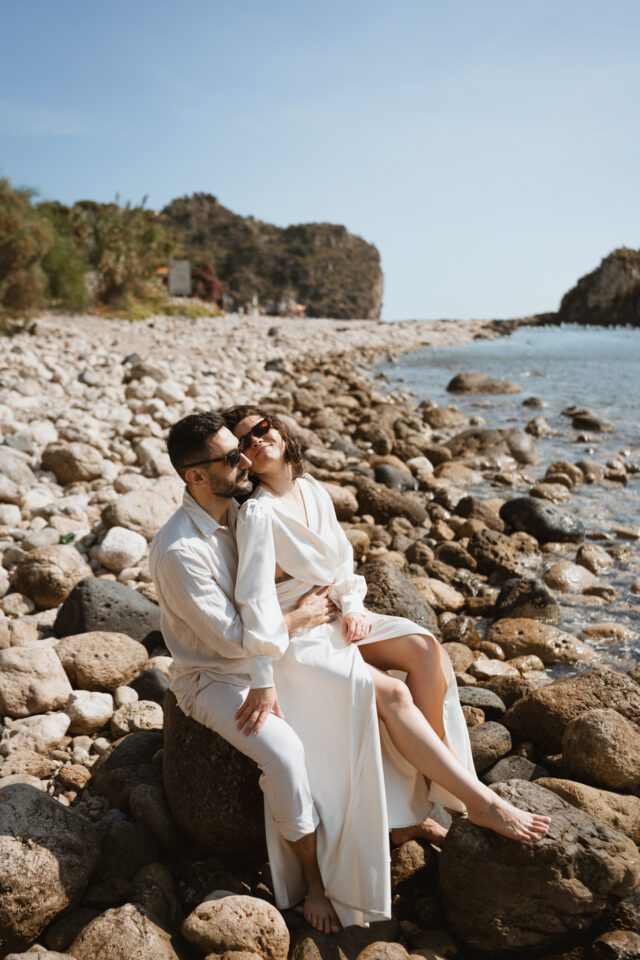 Relaxed couple sitting on rocky shore in Sicily